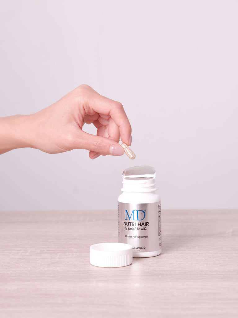 Lifestyle photo showing hand taking one small MD Nutri Hair capsule from bottle—easy to swallow and part of daily scalp health routine

